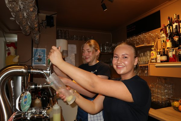 To blide bartendere tapper øl og forbereder drinker bak baren på Sjøbua – livlig atmosfære i Sponvika nær Halden