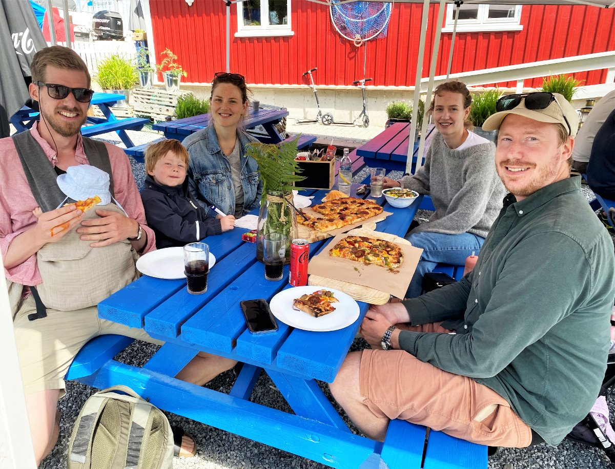 Familie med barn nyter scrocchiarella-pizza på blå benker ute på Sjøbua – familievennlig restaurant ved Ringdalsfjorden nær Halden