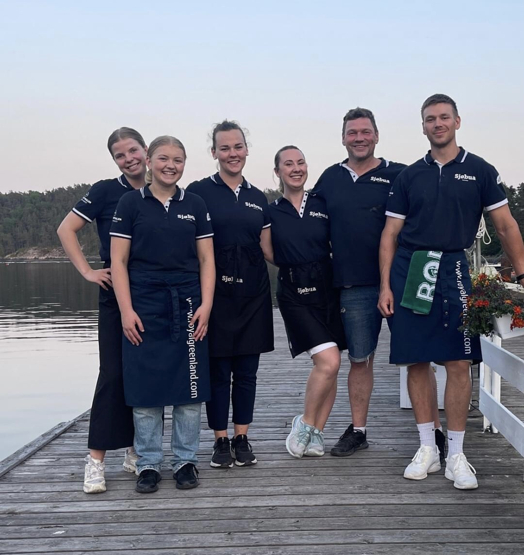 Sjøbua-teamet samlet på brygga i Sponvika – dedikerte medarbeidere i uniform med Royal Greenland-forkle foran Ringdalsfjorden