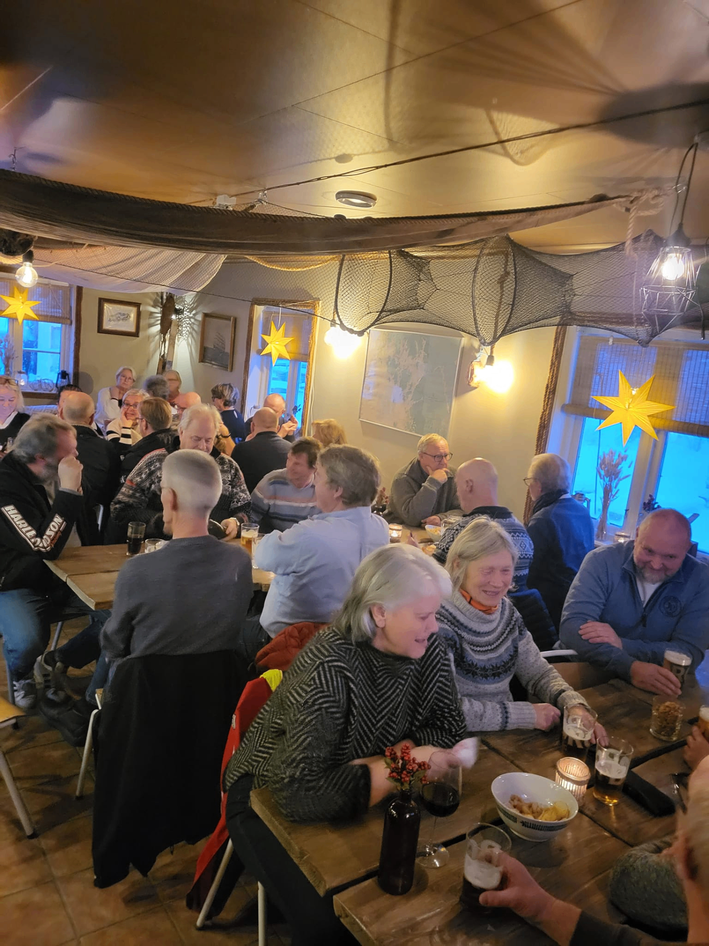 Fullsatt Sjøbua-restaurant med gjester som nyter stemningen – koselig innendørs atmosfære med fiskegarn, sjøstjerner og varmt lys ved Ringdalsfjorden