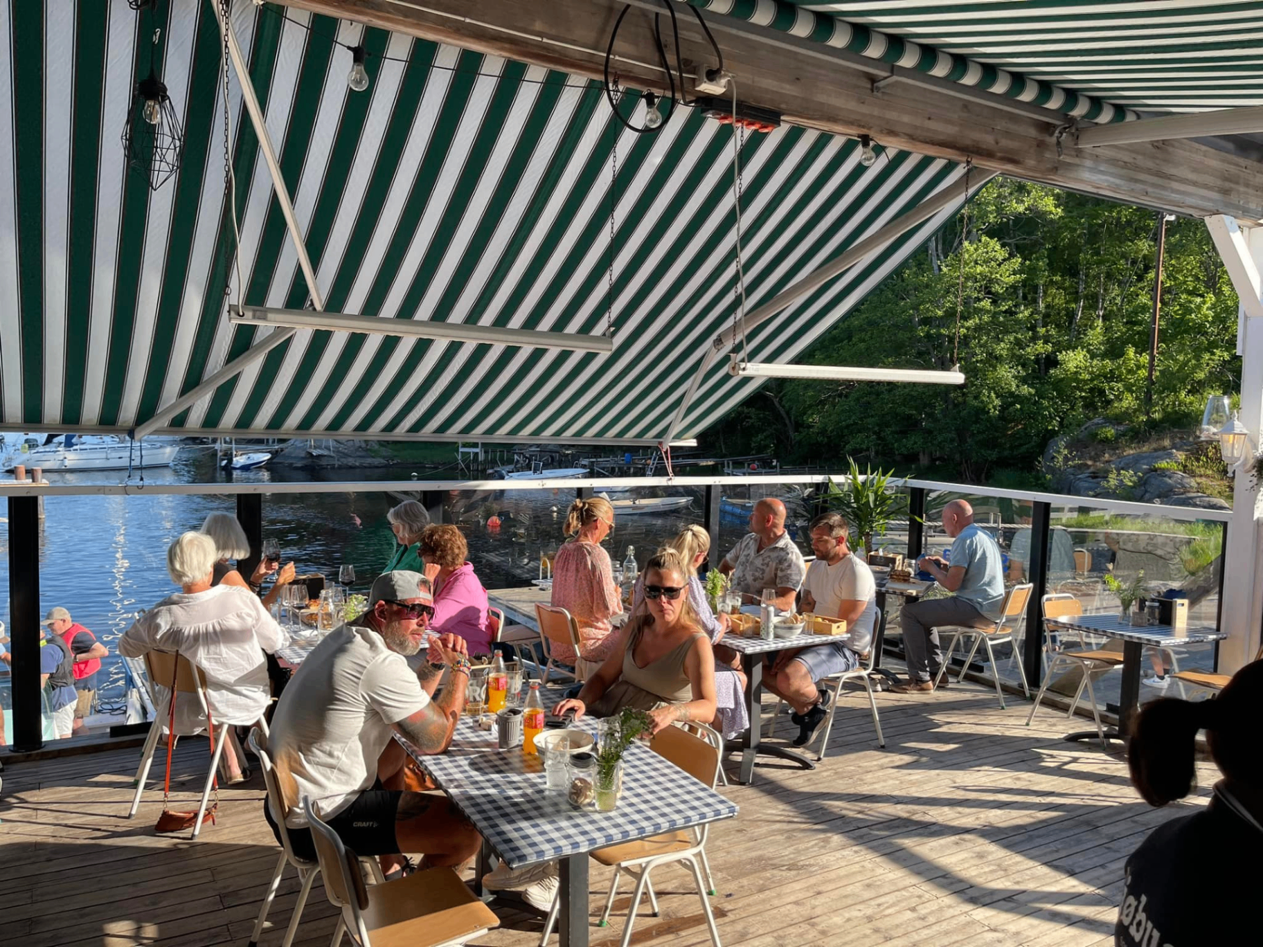 Gjester nyter mat og drikke på Sjøbuas solfylte terrasse med utsikt over båter og Ringdalsfjorden – populær uteservering nær Halden